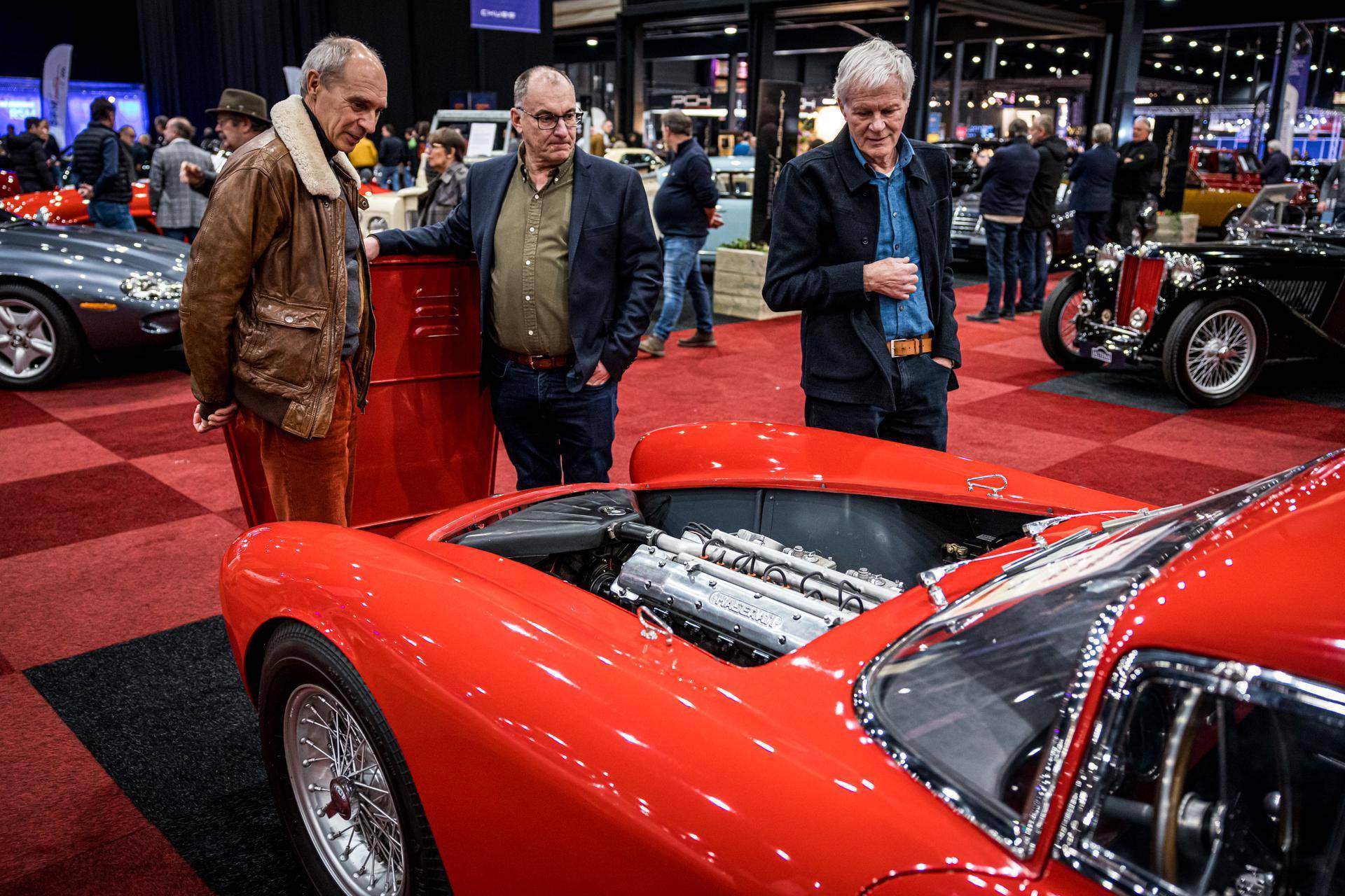 3 men looking at a red Maserati